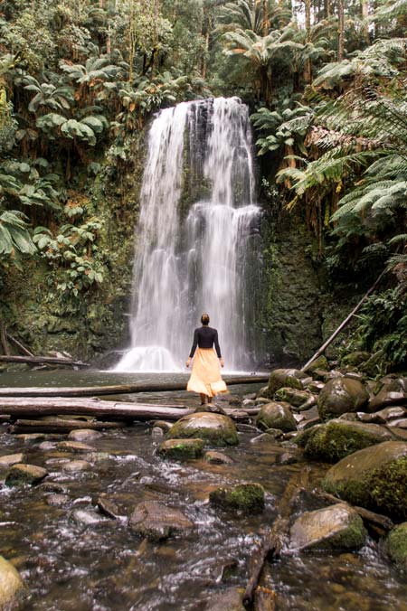 una mujer de pie frente a una cascada rodeada de exuberante selva