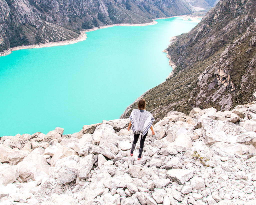 una mujer con poncho blanco de pie frente al lago azul y las montañas