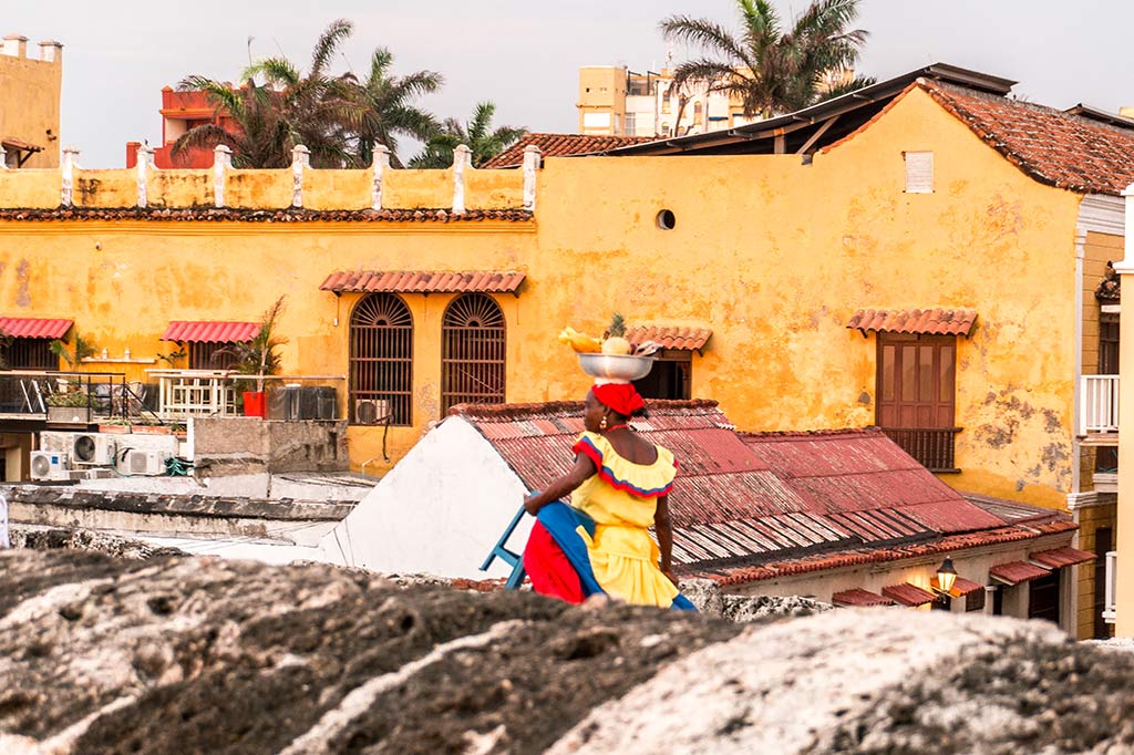 lugar de la lista de cubos de ensueño llamado Cartagena, mujer con un vestido amarillo caminando frente al edificio naranja