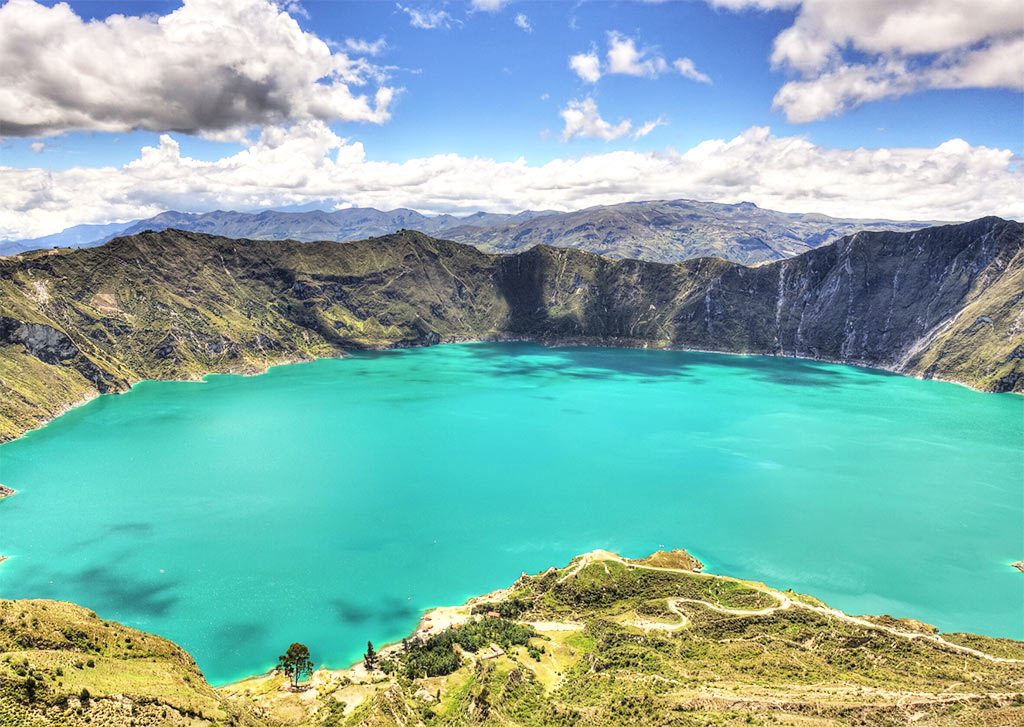 lago con agua turquesa, montañas al fondo y hierba verde en el lago Quilotoa, Ecuador, uno de los destinos de lista de cubos de ensueño más bonitos