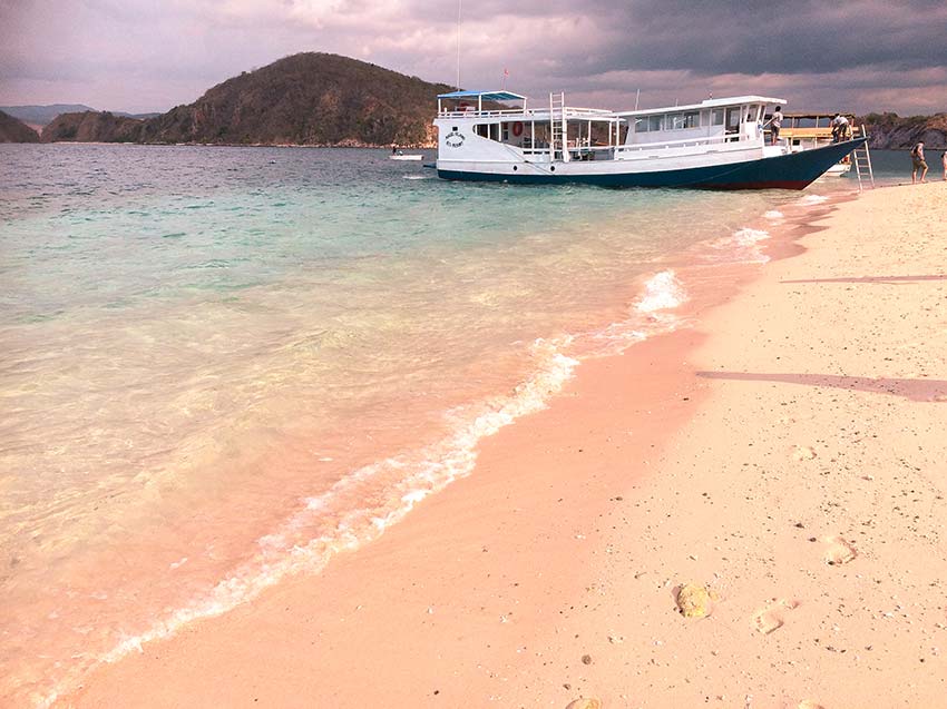 una vista de la playa rosa, las montañas y el barco en la isla de Bidadari 