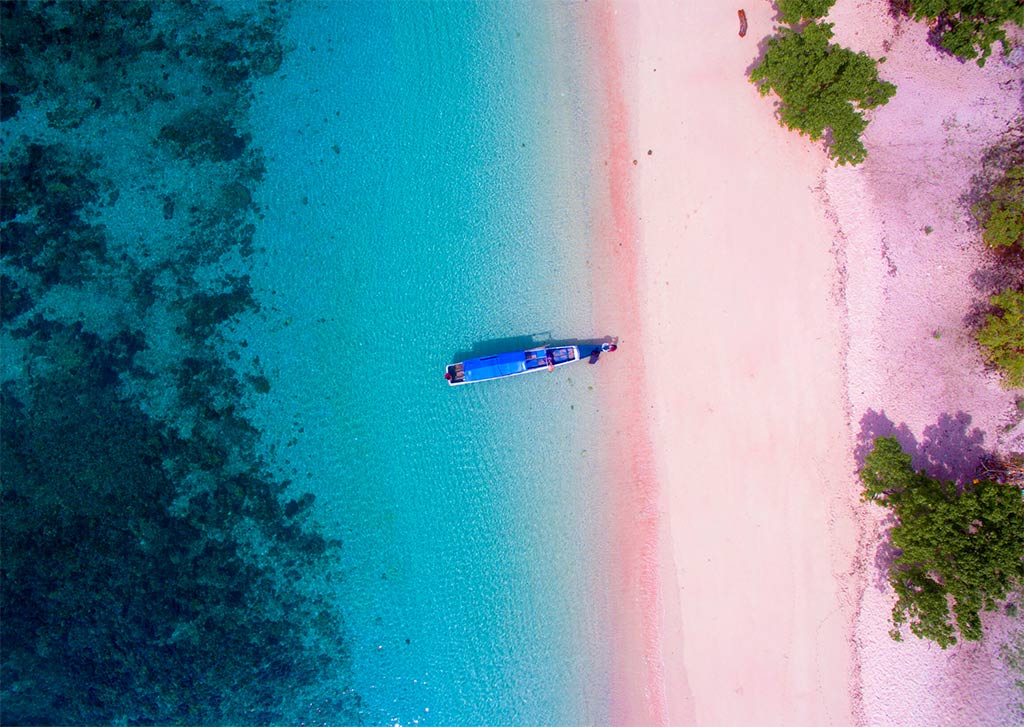 una vista rial de la playa rosa en Indonesia cerca de Labuan Bajo, con un barco y agua turquesa