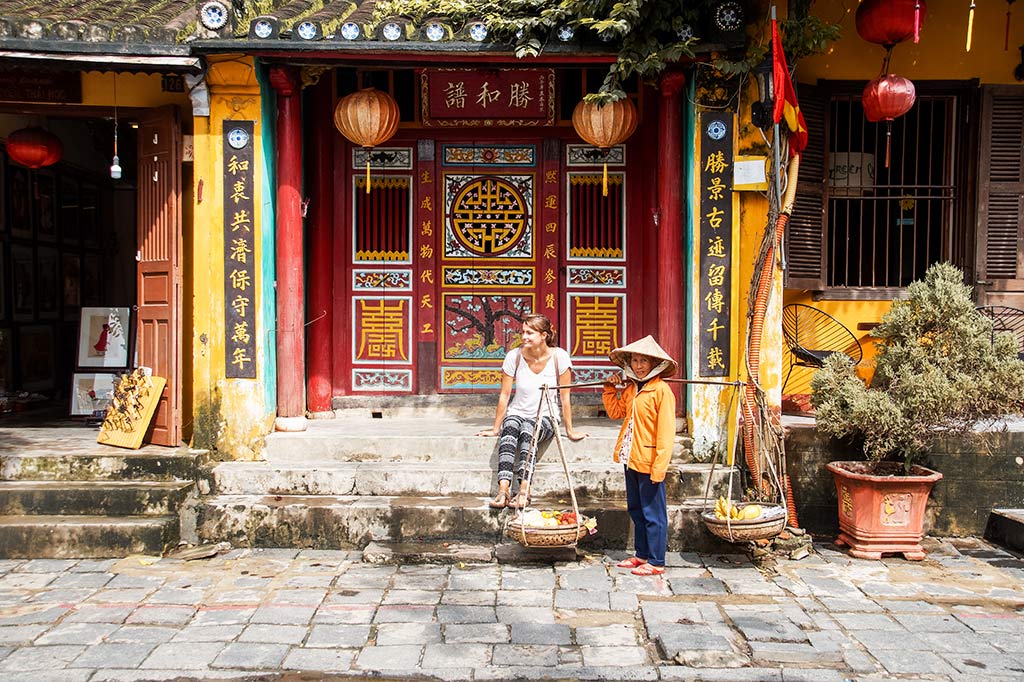 Templo rojo chino, con una chica sentada en las escaleras con la señora vietnamita en Hoi An, Vietnam