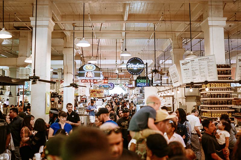 mucha gente en el mercado Grand Central, con muchos letreros de comida que es una de las mejores cosas que hacer en el centro de Los Angeles