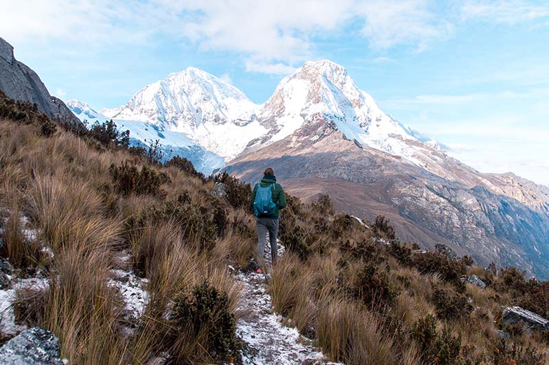 montañas nevadas de Huascaran, y la mujer con mochila azul caminando entre arbusto verde