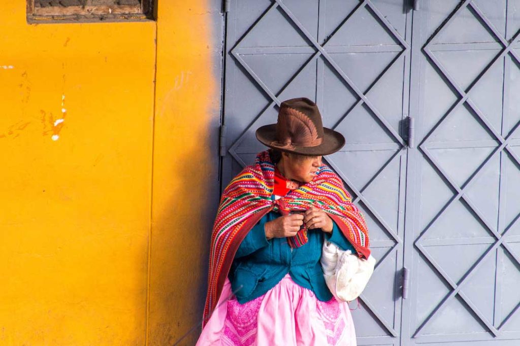 señora peruana con traje tradicional de pie frente a la pared amarilla y gris en Huaraz, Perú