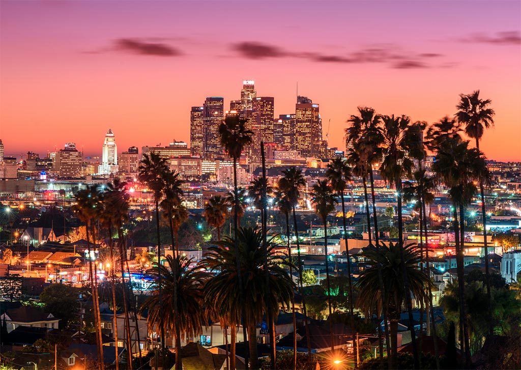 una puesta de sol de observación que es una de las mejores cosas para hacer en el centro de LA, cielo de color naranja rosado, palmeras, rascadores de cielo.