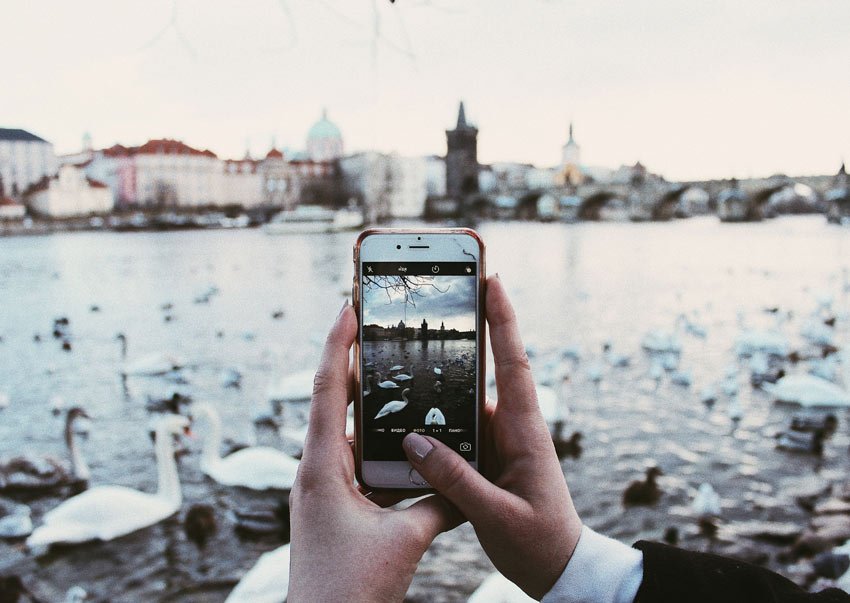 toma de la mano sosteniendo un teléfono con una vista en el río y el puente de Carlos con cisnes alrededor