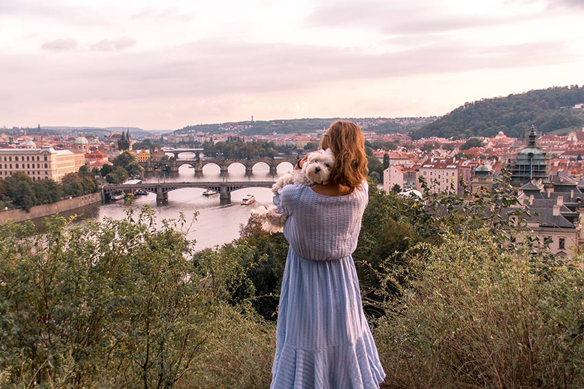 mujer con un vestido azul sosteniendo un día blanco mirando la vista de Praga desde letna hill que es uno de los mejores lugares de fotografía en Praga