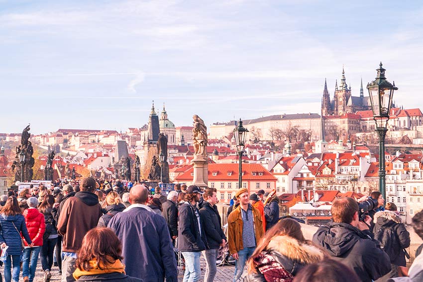 muchas personas caminando en el puente de Carlos que es uno de los lugares de fotos más bellos de Praga