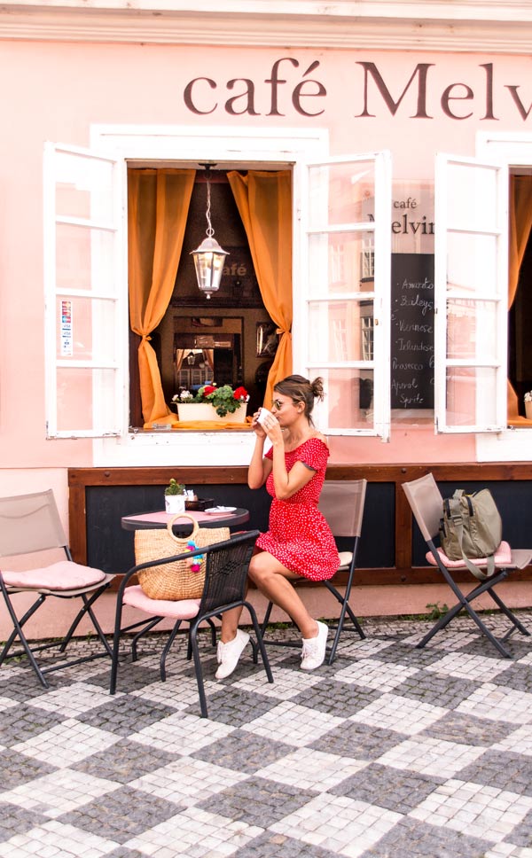 mujer con vestido rojo siting y beber café frente al edificio rosa
