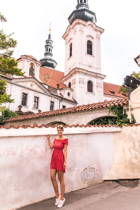 una chica con un vestido rojo de pie frente a la iglesia en Praga, el mejor lugar de fotos 