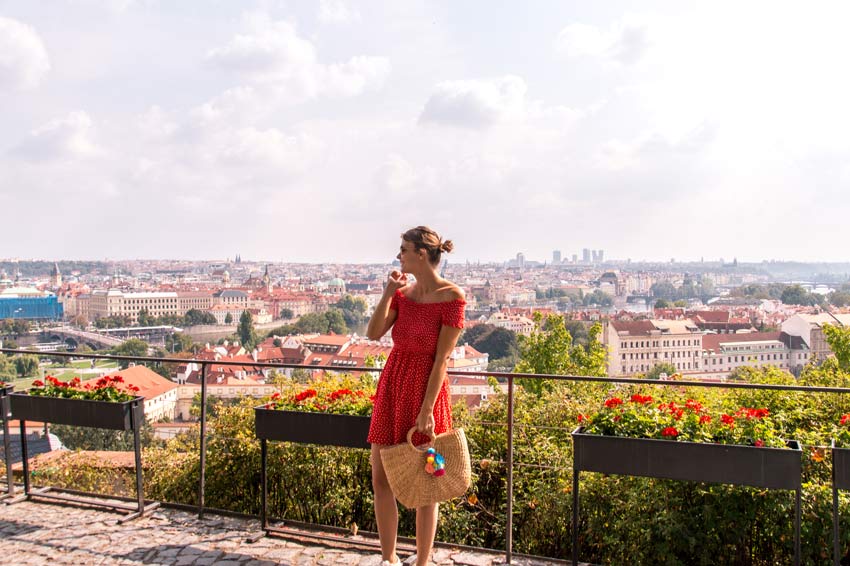 mujer con vestido rojo frente a la hierba verde con vistas a Praga